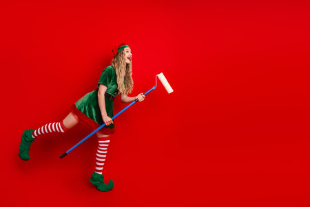 Festive elf character painting a vivid red background with a roller, celebrating the Christmas season with bright cheerの写真素材