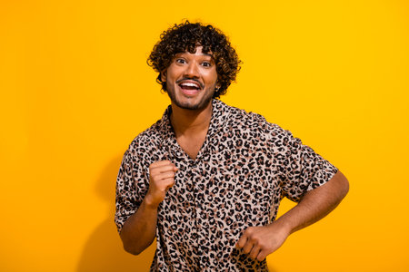 Cheerful young man in leopard print shirt posing against yellow background with energizing charm and enthusiasmの写真素材