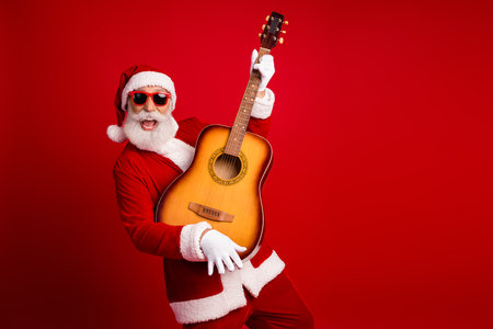 Festive Santa Claus playing a guitar while celebrating Christmas in a joyful holiday mood against a vibrant red backgroundの写真素材