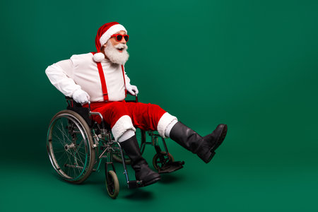 Festive Santa Claus Laughing in a Wheelchair Wearing Funky Sunglass, Celebrating Christmas in Joyful Red Costumeの写真素材