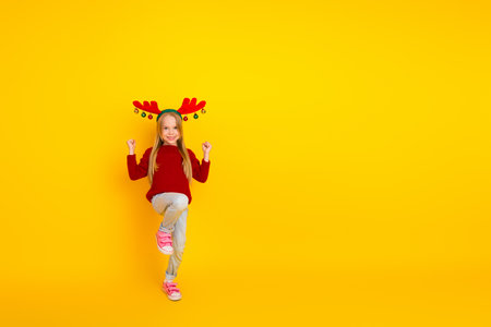 Funny little Christmas kid sparkles with red sweater antler headband on a bright yellow wall cheerful holiday moment for photo lovers and shoppersの写真素材