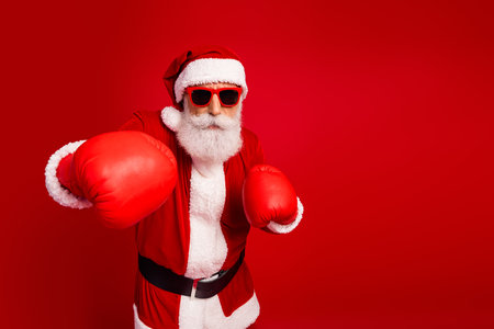 Santa Claus in boxing gloves posing with a festive spirit in front of a red background during holiday seasonの写真素材