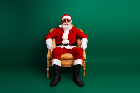 Santa Claus in sunglass sitting on a golden chair against a green background, exuding cool and merry holiday vibesの写真素材