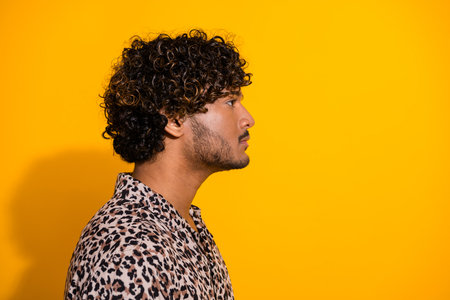 Side profile of a stylish young man with curly hair against a vibrant yellow backgroundの写真素材