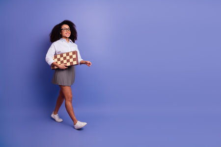 Young woman with afro hairstyle holding a checkered game board while confidently walking in a professional styleの写真素材