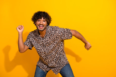 Cheerful young man in leopard print shirt enjoying joyful moment on yellow background in casual styleの写真素材