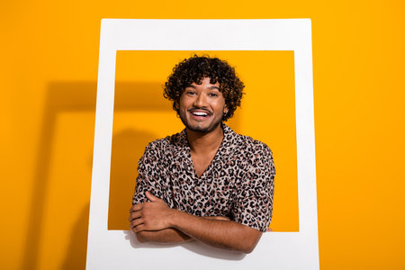 Portrait of a cheerful young man in a leopard print shirt with vibrant yellow background exuding...