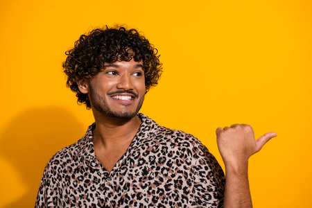 Smiling young man in a leopard print shirt gesturing with his hand against a vibrant yellow backgroundの写真素材