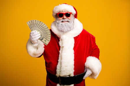 Santa Claus in vibrant costume holding money and wearing sunglass, posing with a cheerful smile...