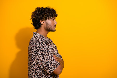 Profile of a stylish young man in leopard print shirt against a vibrant yellow background with crossed armsの写真素材