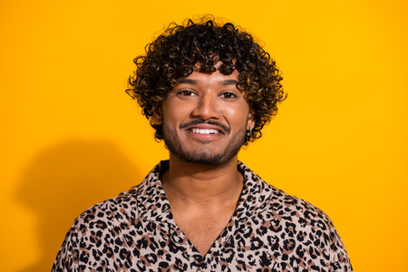 Happy young man on a yellow background wearing a leopard print shirt, smiling confidently and showcasing trendy fashionの写真素材