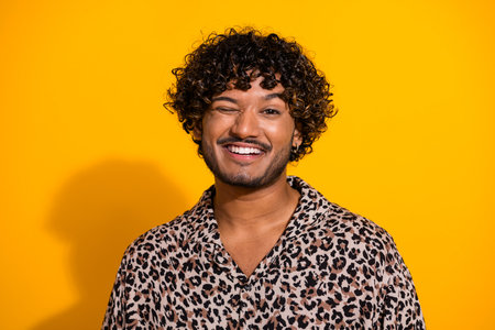 Young man in leopard print shirt poses against yellow background with a cheerful smile showcasing a stylish fashion lookの写真素材