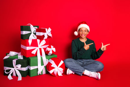 Joyful young boy celebrates Christmas with festive gifts and Santa hat in a cheerful red winter holiday settingの写真素材