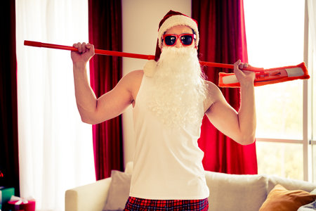 Funny Santa Claus in casual wear holding a mop in a cozy home interior, celebrating a relaxed Christmas with styleの写真素材