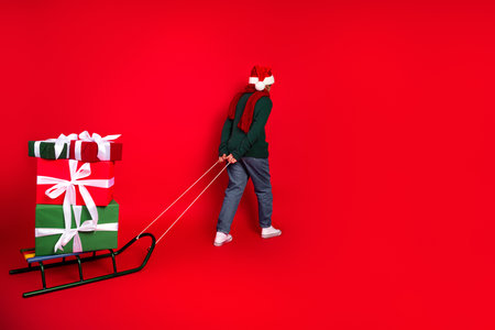 Child Pulling Sled with Colorful Presents Against Vibrant Red Christmas Backgroundの写真素材