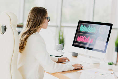 Businesswoman Analyzing Data on a Computer in a Modern Office Setting, Emphasizing Financial and Professional Tasks in a Stylish Interiorの写真素材