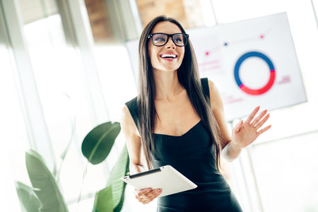 Young happy businesswoman presenting office report holding tablet in modern workspace indoor with cheerful enthusiasmの写真素材