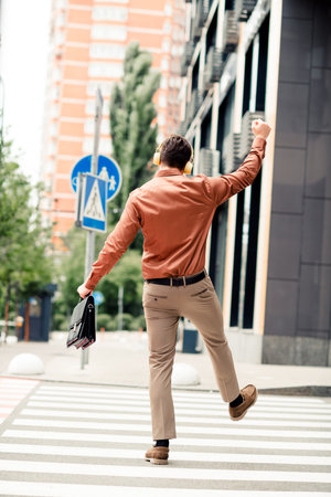 Young professional businessman crossing an urban street while enjoying music on headphones, representing a modern and confident lifestyle.の写真素材