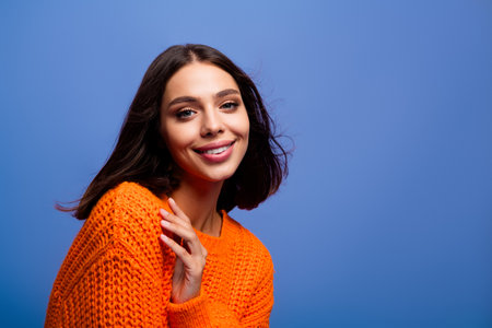 Portrait of a young woman wearing a bright orange sweater with a cheerful smile, posing against a vibrant blue background.の写真素材