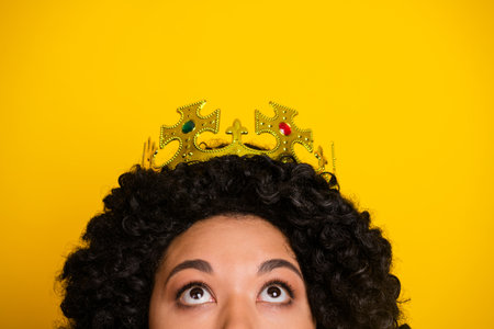 Closeup of a person with a crown and curly hair against a vibrant yellow backdrop, evoking royalty and charmの写真素材