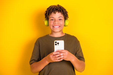 playful boy with green headphones holds a phone smiles against a bright yellow background for casual style promoの写真素材
