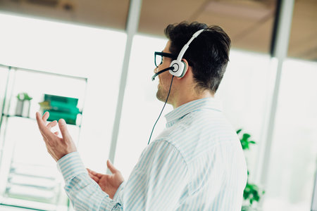 Businessman wearing a headset conducting a professional online meeting in a modern officeの写真素材