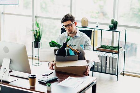 Professional man at an office desk with a box containing personal items symbolizing reflection and career change.の写真素材
