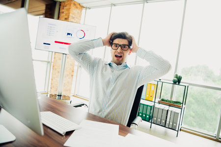 Frustrated businessman holding head in office after viewing data on screen due to workplace stress and tensionの写真素材