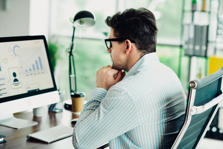 Young business professional working on analytics at office desk, analyzing charts and data on a computer screenの写真素材