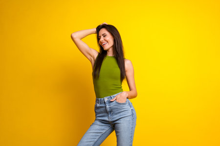 Charming girl showing a joyful smile while posing stylishly on a vibrant yellow background in casual outfit and green topの写真素材