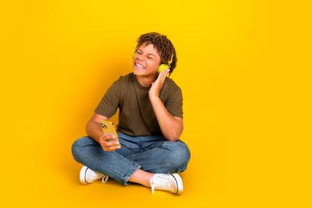 Playful teen with headphones enjoys music on the go against a bright yellow background in casual styleの写真素材