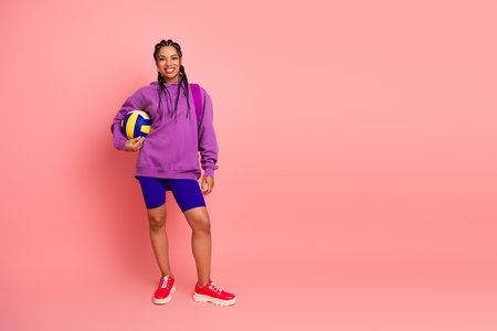 Athletic woman in vibrant sportswear holding a volleyball, posing against a pink background showcasing fitness and styleの写真素材