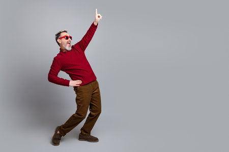 Handsome middle-aged man pointing upward wearing a red sweater and trendy glasses against a solid gray backgroundの写真素材