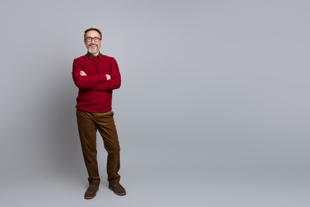 Confident mature man standing arms crossed against a clean background wearing casual attire including pullover and pantsの写真素材