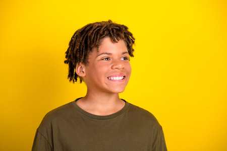 Funny cheerful boy with dreadlocks smiles against bright yellow background in casual khaki tshirt for joyful lifestyle adの写真素材