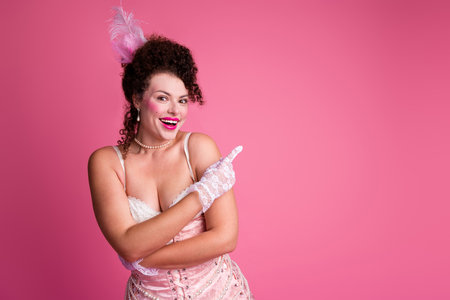 Elegant woman in vintage attire with delightful smile and playful pose against vibrant pink background, showcasing classic glamourの写真素材