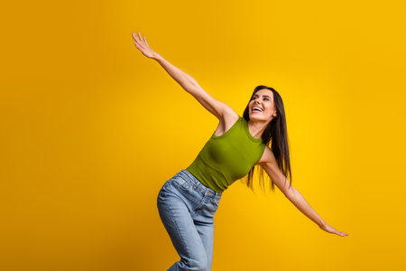 Smiling woman in casual attire posing playfully with a vibrant yellow background creating a cheerful and lively moodの写真素材