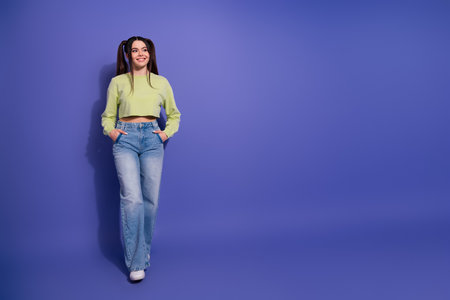 Stylish young woman with ponytails in casual outfit posing confidently with a vibrant purple background highlighting her charmの写真素材