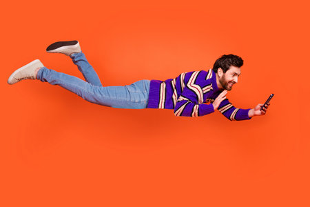 Full length photo of handsome young guy flying video call wave hand dressed stylish striped purple garment isolated on orange backgroundの写真素材