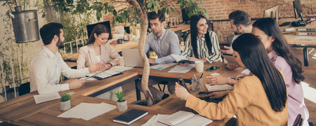 Photo of business men ladies seven people partners sitting around table desktop spacious big office members successful professionals company good mood discussing new project indoorsの写真素材