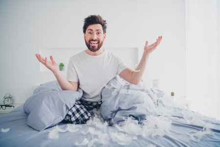 Full size photo of attractive young male play fluffy bird feathers sit bed dressed sleepwear wake up cozy day light home interior bedroomの写真素材