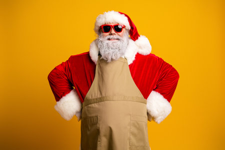 Funky Santa Claus in a trendy apron standing confidently with sunglasses on a vibrant yellow backgroundの写真素材