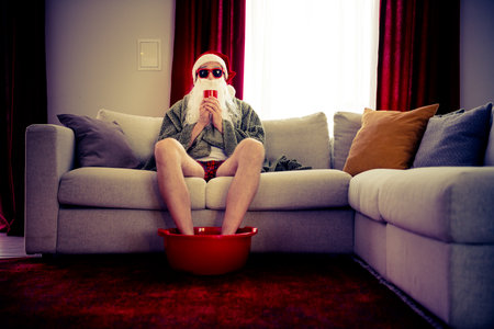 Relaxed Santa Claus lounging with feet soaking, enjoying a cozy festive home atmosphereの写真素材