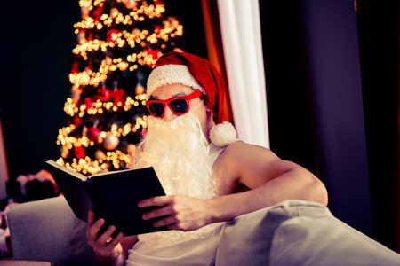 Santa Claus Relaxing in Pajamas While Reading at Home During a Merry Christmas Winter Celebrationの写真素材