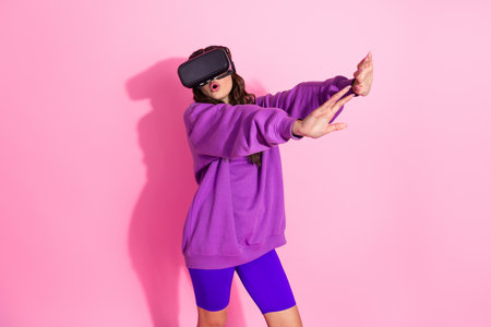 Young woman in trendy sportswear experiencing virtual reality with headset against a vibrant pink...