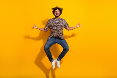 Young stylish man posing playfully midair against bright yellow background in trendy outfit