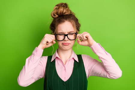 Young woman in glasses wearing school uniform making a pensive gesture while posing against a vibrant green backdropの写真素材