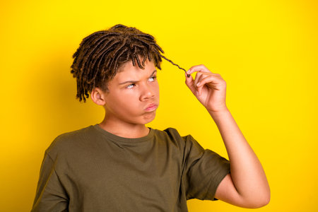 Vivid portrait of a young multiethnic boy with dreadlocks pulling a strand against a bright yellow background showcasing casual fashion and playful curiosityの写真素材