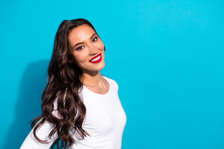 Smiling young woman in casual white pullover against a vibrant blue backdrop showcasing beauty and charmの写真素材