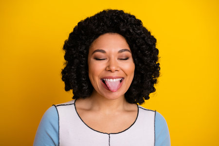 Joyful woman making a playful face with a yellow background highlighting her cheerful personality and positivityの写真素材